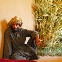 A Pashtun tribesman sits inside his simple mud brick adobe next to his family\'s harvest of corn