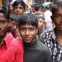 Three boys posing for picture in the middle of a crowded street, Dhaka