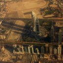 Tall buildings throw their shadows far across the landscape, as seen here from the air. A camel and horse race track is visible in the upper portion of the photo.