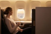 A passenger in a private business-class suite enjoys a glass of champagne while looking out the window at a sunset, emphasizing a serene journey.
