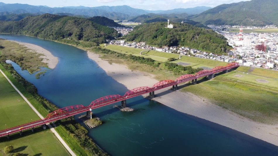 Aerial view of a red arched bridge over the Shimanto River surrounded by mountains, Kochi, Japan
